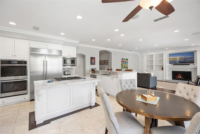 kitchen with visible vents, arched walkways, a kitchen island, built in appliances, and a sink