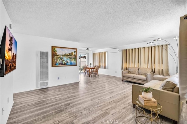 living room featuring visible vents, a ceiling fan, an AC wall unit, a textured ceiling, and wood finished floors