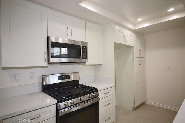 kitchen with light countertops, light tile patterned flooring, white cabinets, a raised ceiling, and appliances with stainless steel finishes