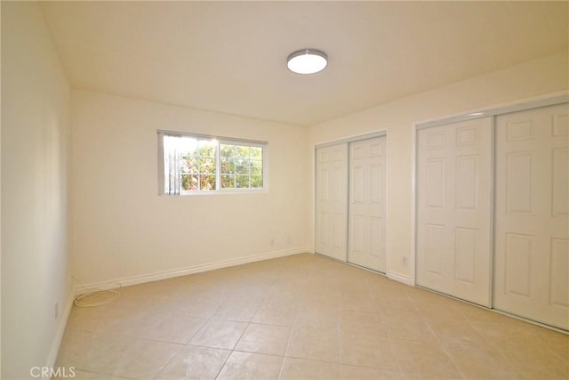 unfurnished bedroom featuring two closets, light tile patterned floors, and baseboards