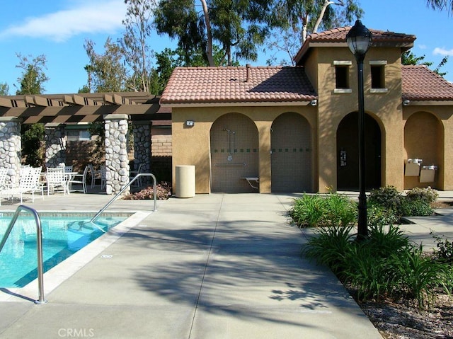 view of front of property featuring stucco siding, a patio area, a community pool, a pergola, and a tiled roof