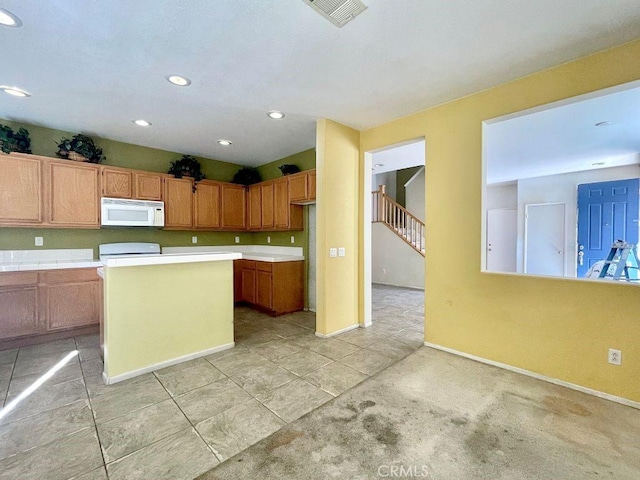 kitchen featuring baseboards, visible vents, white microwave, a kitchen island, and stove