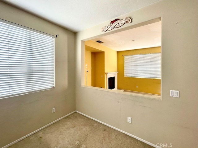 empty room with carpet, a fireplace, visible vents, and baseboards