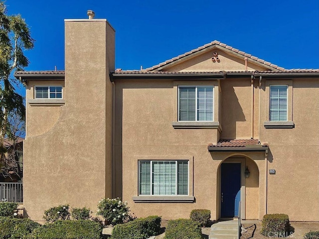 view of front of house featuring a tiled roof, a chimney, and stucco siding