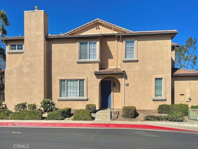 mediterranean / spanish home with a tiled roof, a chimney, and stucco siding