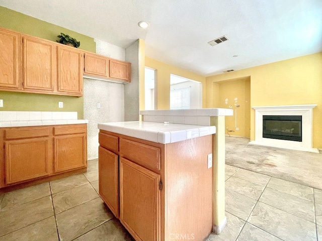 kitchen featuring light tile patterned floors, tile counters, visible vents, a glass covered fireplace, and open floor plan