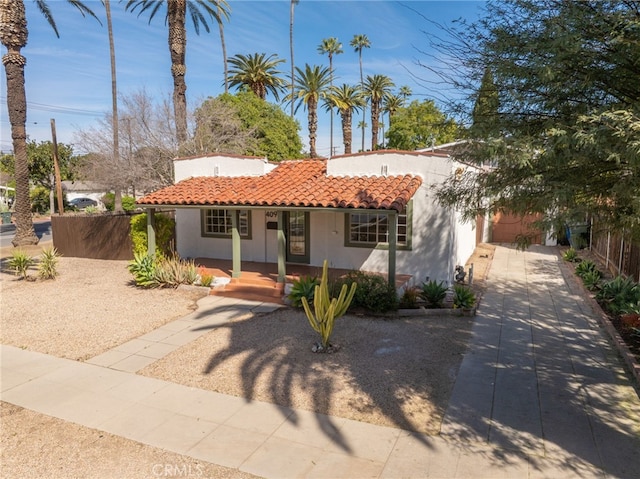 mediterranean / spanish house featuring covered porch, a tile roof, fence, and stucco siding