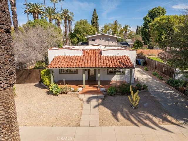 back of house with stucco siding, fence, a porch, and a tiled roof