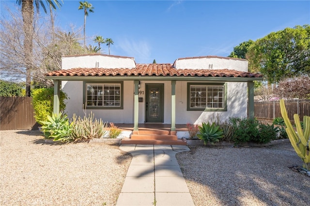 mediterranean / spanish house with covered porch, a tile roof, fence, and stucco siding