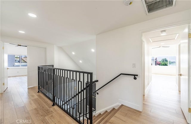 hall featuring light wood finished floors, baseboards, visible vents, and an upstairs landing