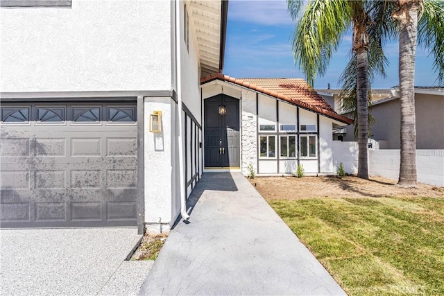 doorway to property featuring a garage, a tiled roof, fence, and stucco siding