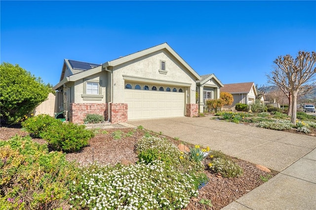 view of front of home featuring an attached garage, brick siding, concrete driveway, roof mounted solar panels, and stucco siding