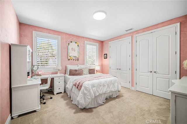 bedroom with light colored carpet, visible vents, and two closets