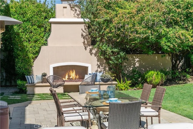 view of patio / terrace with a warm lit fireplace, outdoor dining space, and a fenced backyard