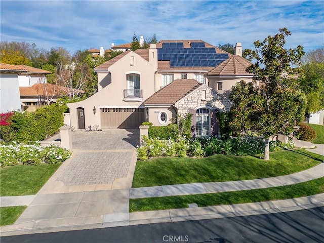 view of front of property featuring a balcony, stone siding, stucco siding, decorative driveway, and a front yard