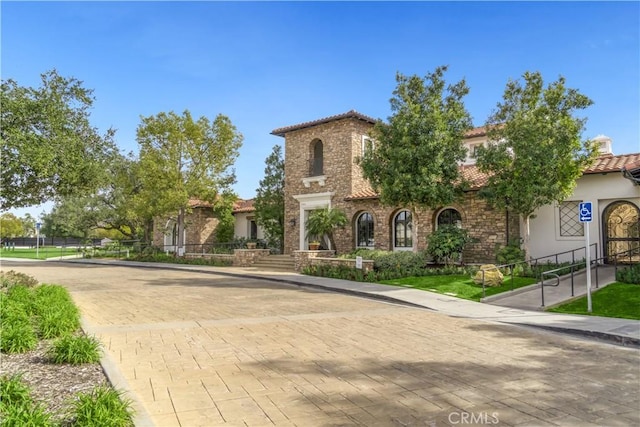 mediterranean / spanish-style home featuring fence, a tiled roof, and stucco siding