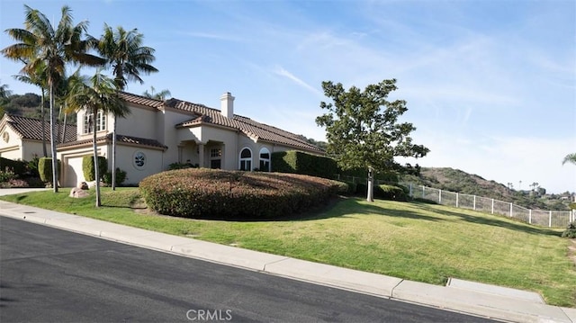 mediterranean / spanish house featuring fence, a tile roof, stucco siding, a chimney, and a front yard