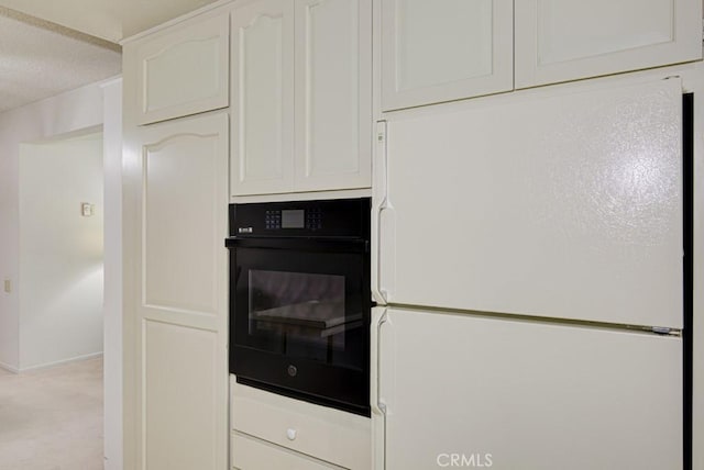 kitchen featuring light carpet, black oven, white cabinetry, and freestanding refrigerator