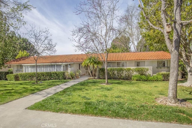 ranch-style home with a tile roof, a front lawn, and stucco siding