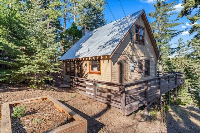 view of side of home with metal roof, a chimney, a wooden deck, and a garden