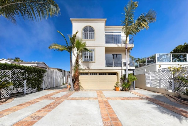 view of front of house with stucco siding, concrete driveway, an attached garage, fence, and a balcony