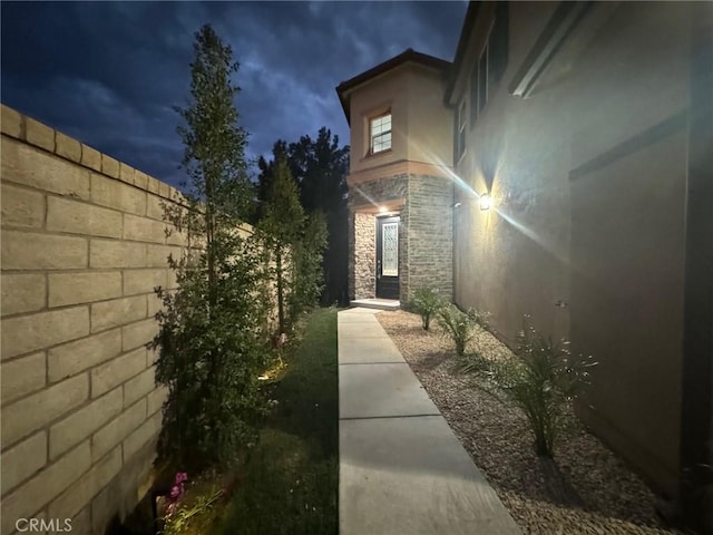 exterior space featuring stone siding, fence, and stucco siding