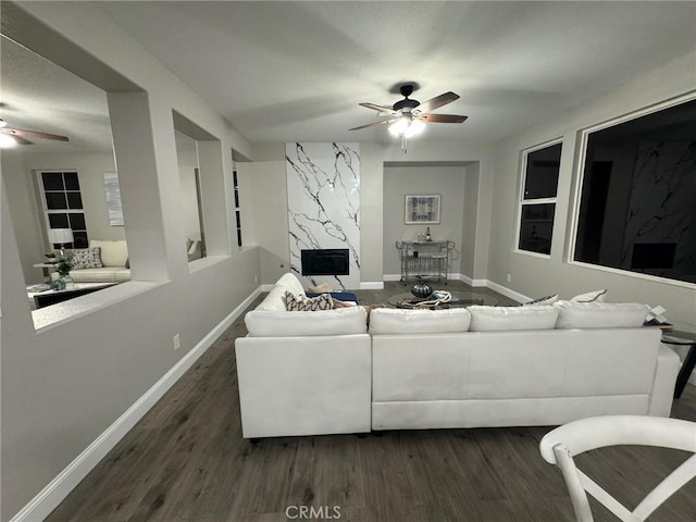 living area with baseboards, a ceiling fan, and dark wood-type flooring