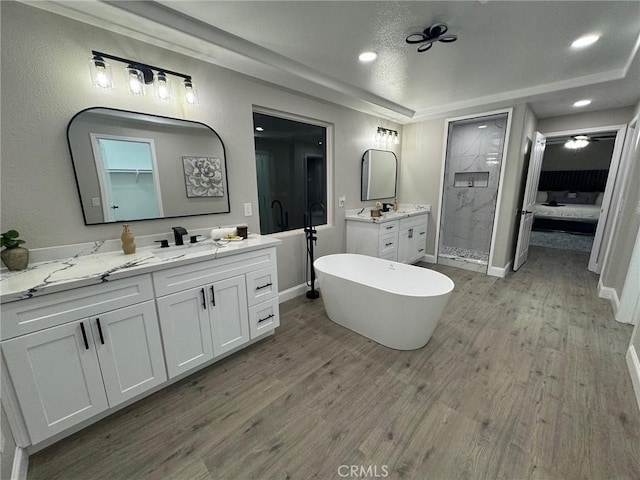 ensuite bathroom with two vanities, wood finished floors, a freestanding tub, a shower stall, and a sink