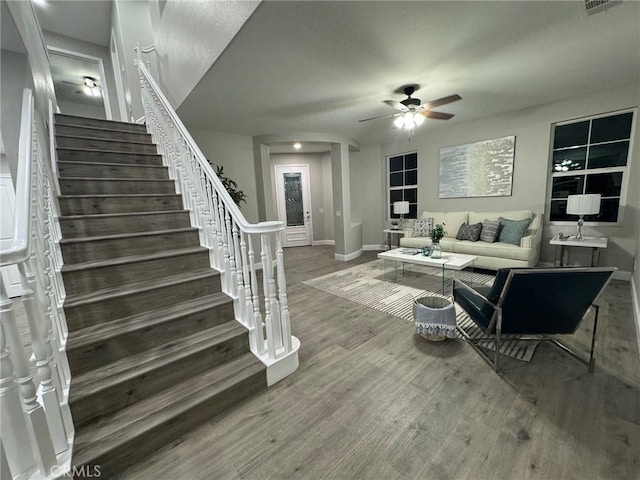 living area featuring stairway, wood finished floors, a ceiling fan, and baseboards