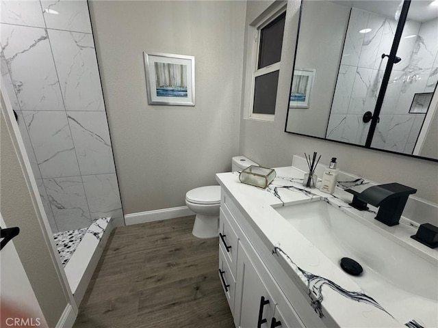 bathroom with a marble finish shower, toilet, vanity, wood finished floors, and baseboards