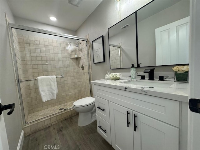 bathroom featuring toilet, wood finished floors, vanity, visible vents, and a shower stall