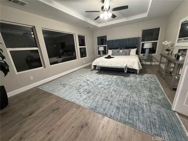 bedroom featuring baseboards, visible vents, a tray ceiling, and wood finished floors