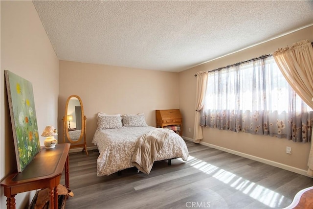 bedroom with a textured ceiling, baseboards, and wood finished floors