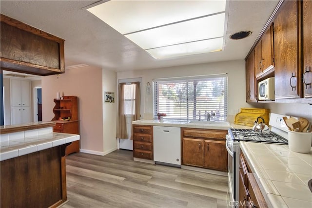 kitchen with tile countertops, white appliances, light wood finished floors, and a sink