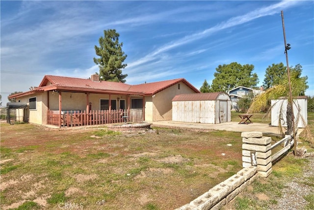 view of front of home with an outbuilding, stucco siding, a shed, a chimney, and a patio area