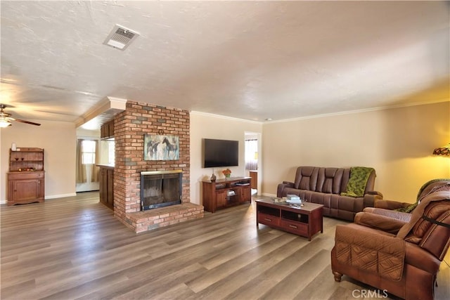 living room with a brick fireplace, crown molding, visible vents, and wood finished floors