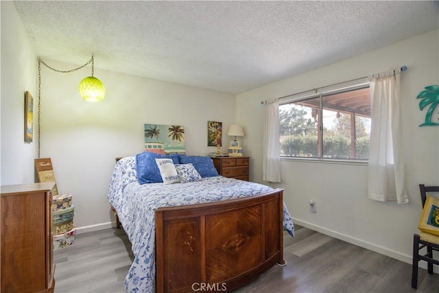 bedroom with a textured ceiling, baseboards, and wood finished floors