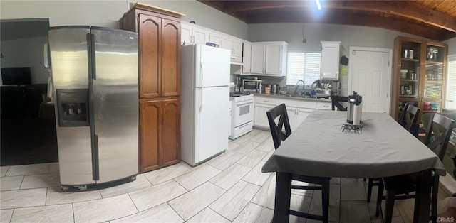 kitchen with a sink, white cabinetry, stainless steel appliances, and beam ceiling