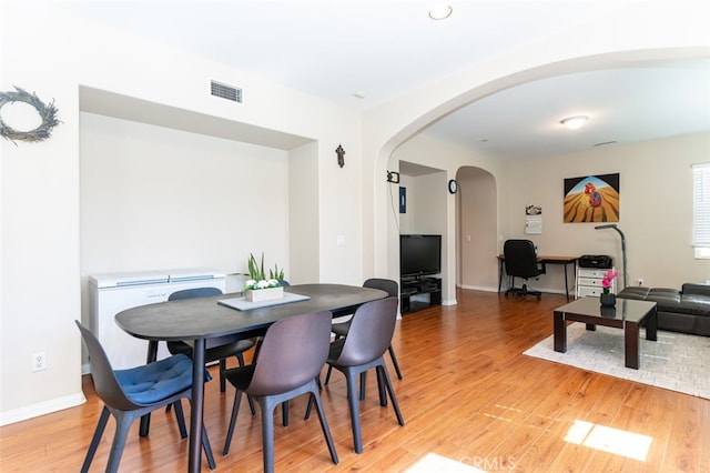 dining space with arched walkways, light wood finished floors, visible vents, and baseboards