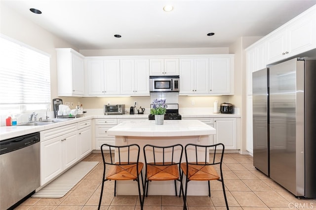 kitchen with tile countertops, appliances with stainless steel finishes, a sink, and white cabinets