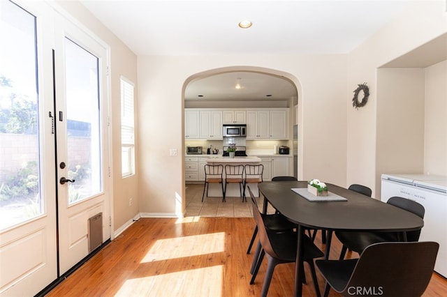 dining space featuring arched walkways, a healthy amount of sunlight, baseboards, and light wood-style floors