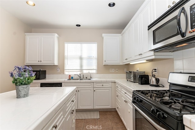 kitchen featuring appliances with stainless steel finishes, tile counters, white cabinetry, and a sink