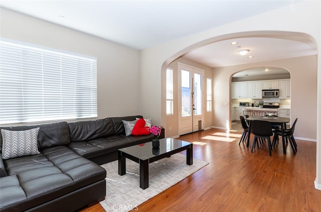 living room featuring arched walkways, recessed lighting, baseboards, and light wood-style floors