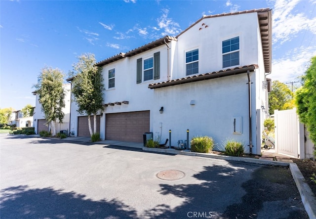 mediterranean / spanish house with a garage, driveway, a tiled roof, and stucco siding