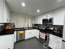 kitchen with stainless steel appliances, dark countertops, a sink, and white cabinets