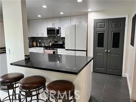 kitchen featuring a breakfast bar, dark tile patterned floors, appliances with stainless steel finishes, backsplash, and dark countertops