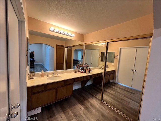 full bathroom with double vanity, a sink, a textured ceiling, and wood finished floors