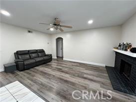 living area with arched walkways, a fireplace with raised hearth, baseboards, and wood finished floors