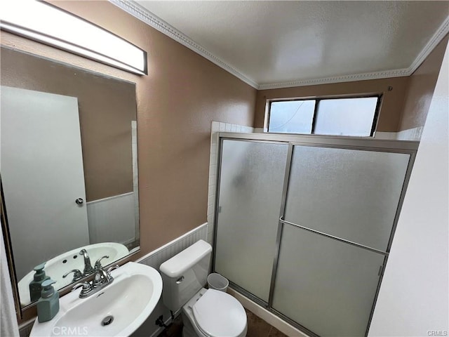 bathroom featuring a stall shower, toilet, a wainscoted wall, crown molding, and a sink