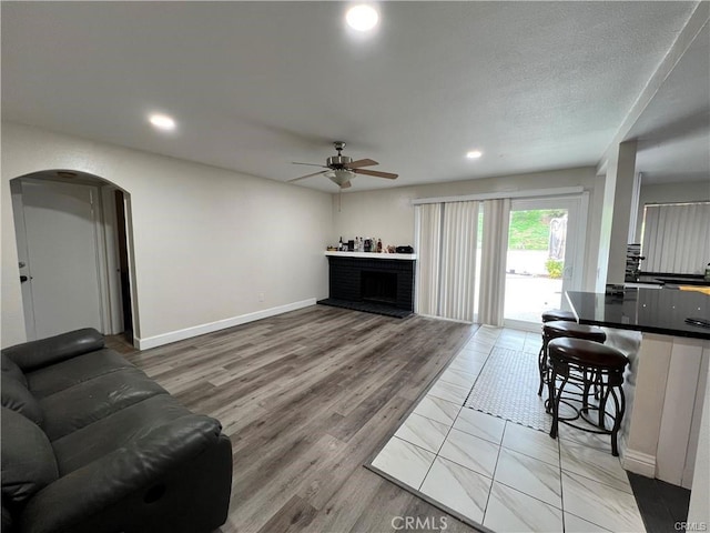 living area featuring arched walkways, a ceiling fan, light wood-type flooring, a fireplace, and recessed lighting